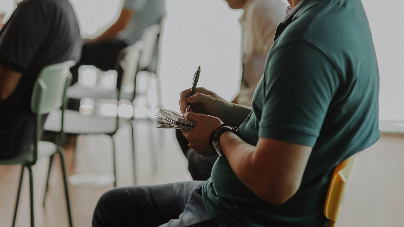 En man sitter i ett klassrum och noterar i sina anteckningar