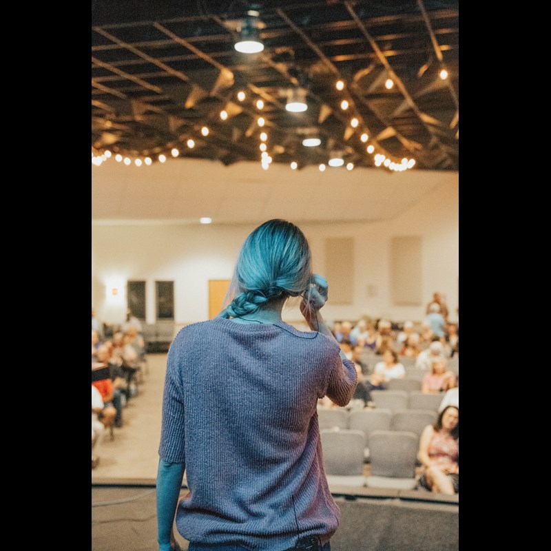 En bild på en kvinna som står på en scen för att hålla en föreläsning för en publik